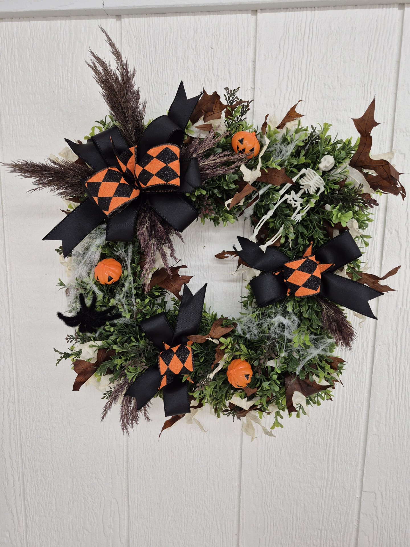 Wreath with orange and black ribbon and small jack-o-lanterns on a white background.