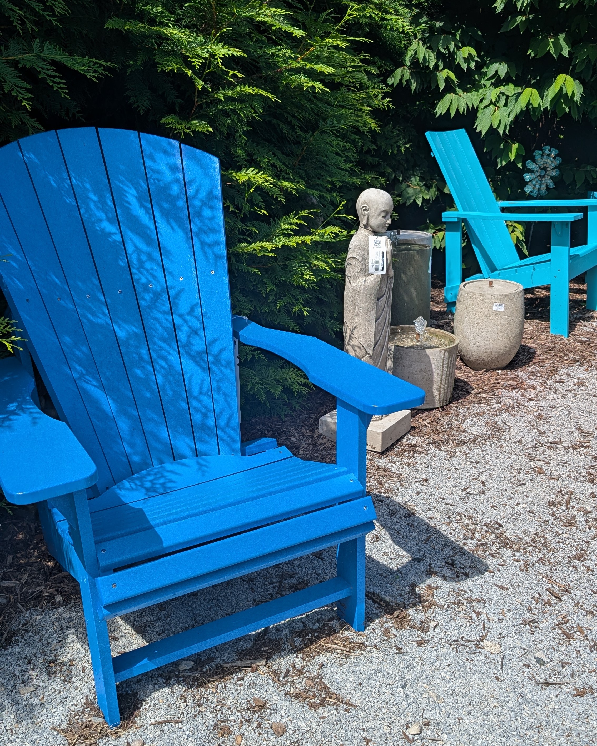 Blue Adirondak chair in foreground, with a tall human figure statue and shorter fountains in the background.