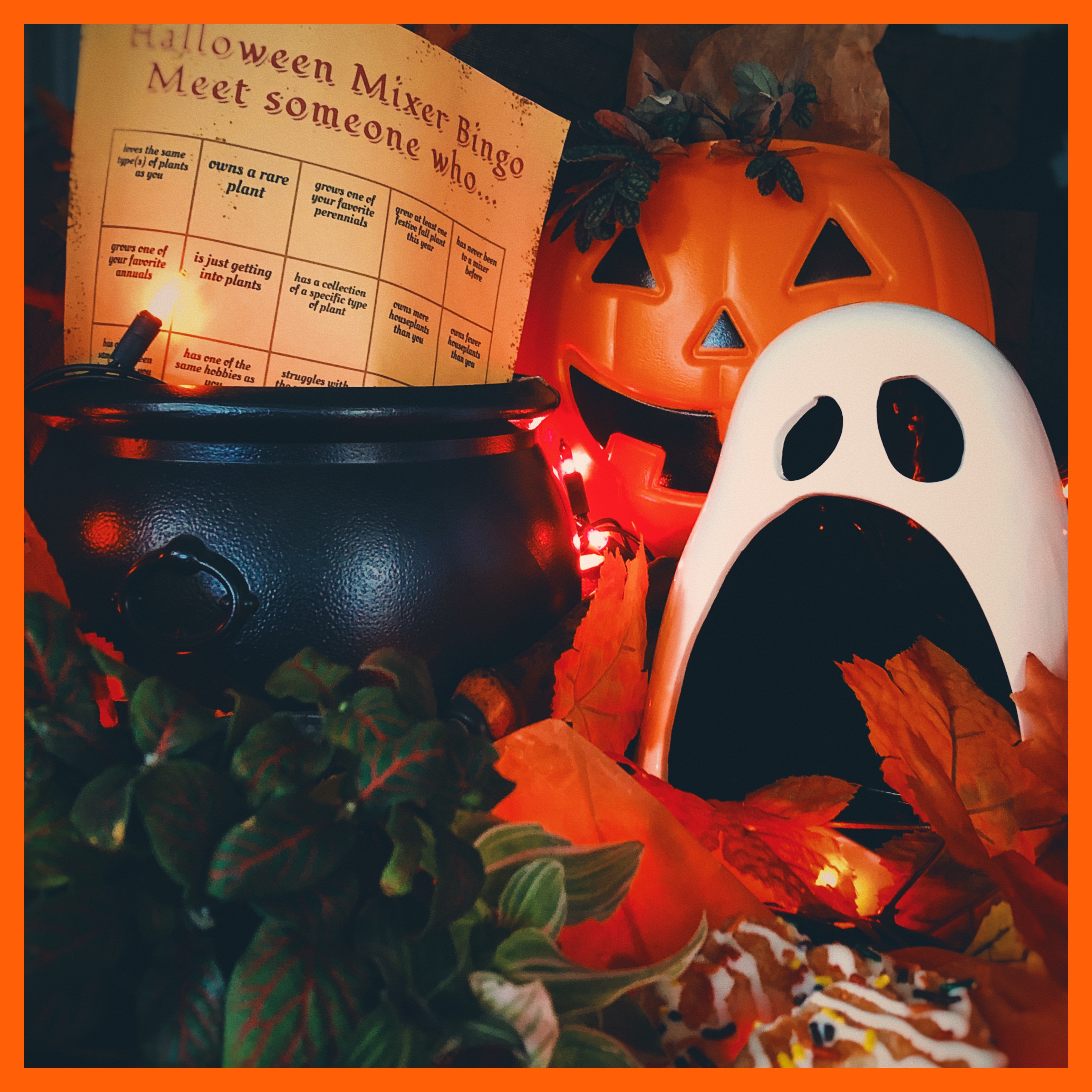 Halloween table scape with a plant in front of a black cauldron on the left, and a ghost figurine in front of a jack-o-lantern bucket.