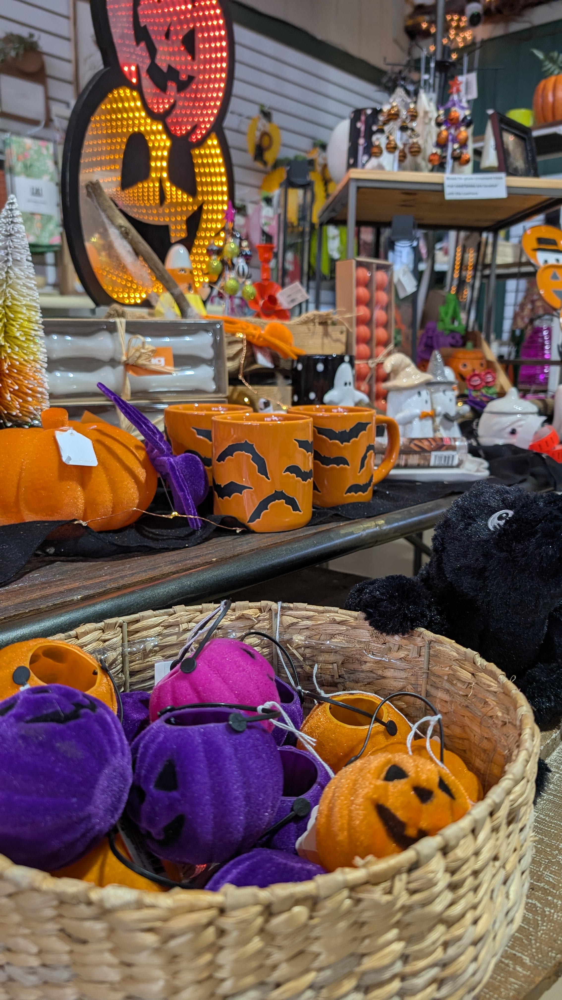 Basket in foreground with purple, orange and pink jack o lanterns, with a light up pumpkin sign and orange pumpkins and mug in the background.