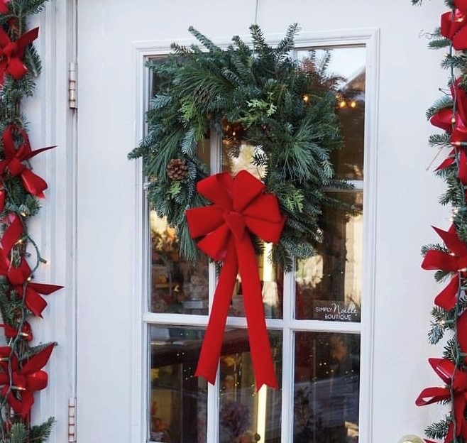 Green wreath with a red bow on a white door with glass panels.