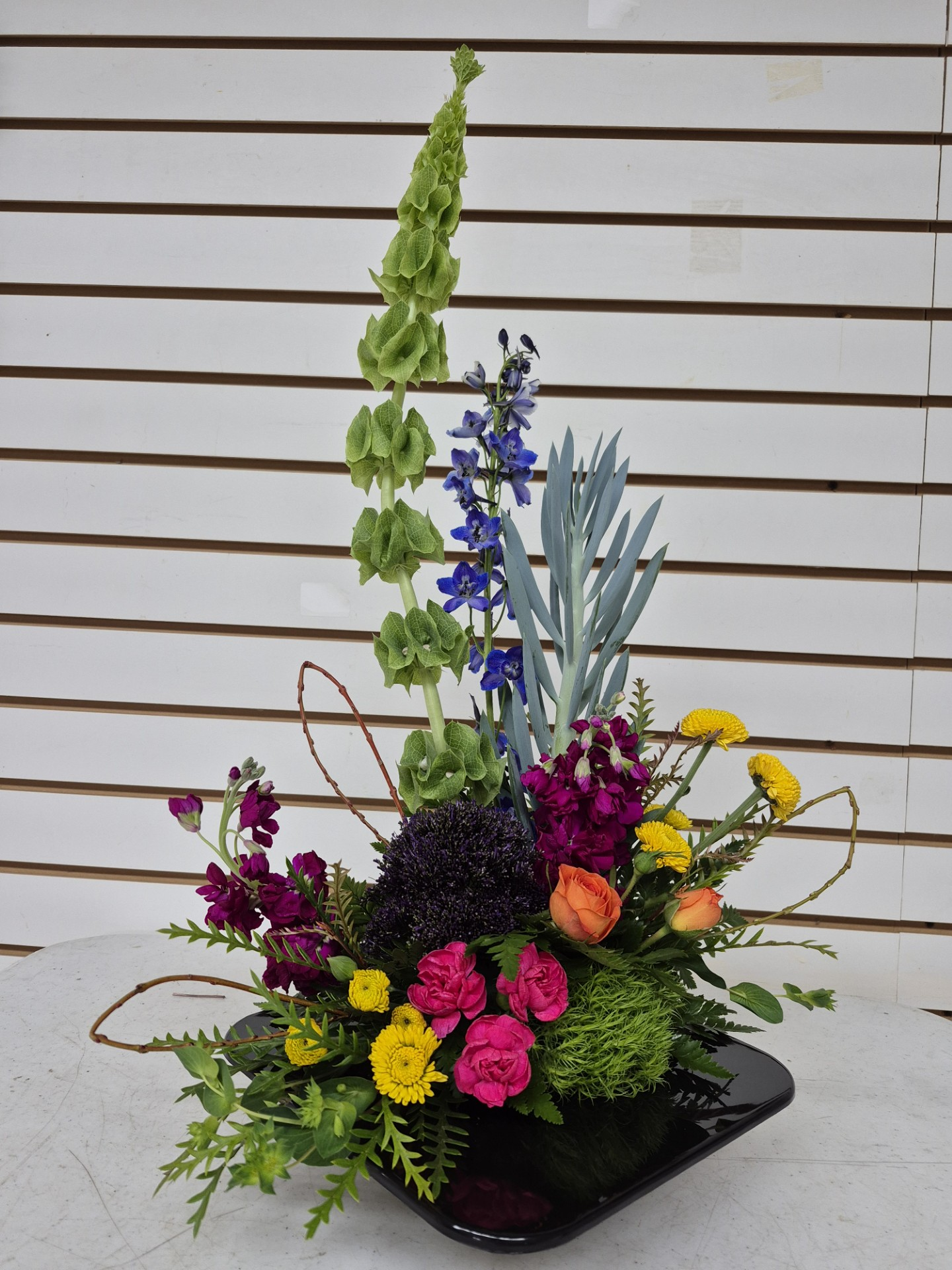 White background with a tall succulent and flower arrangement in a black container.