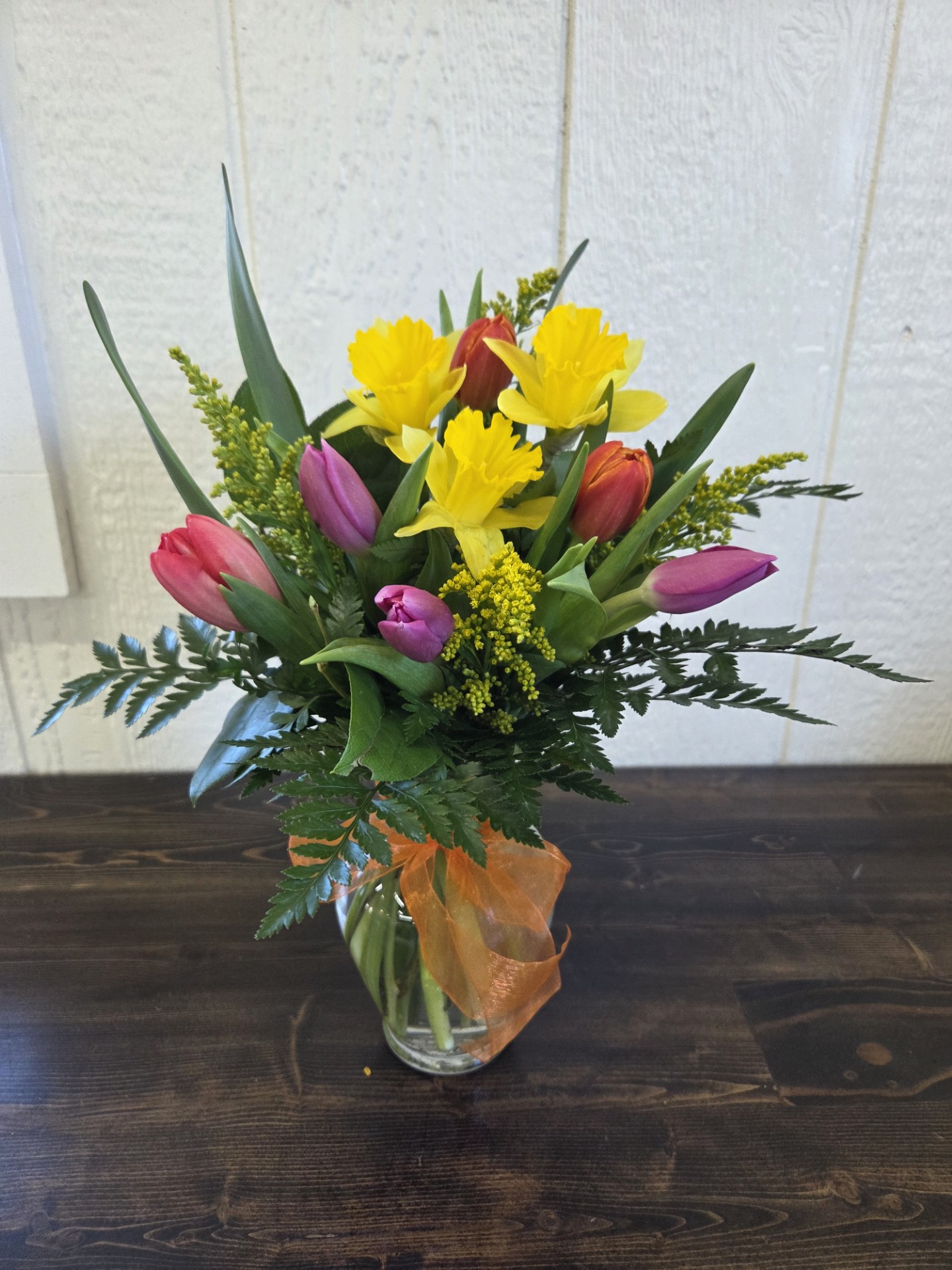 Clear glass vase on a wooden counter with tulips and daffodils.