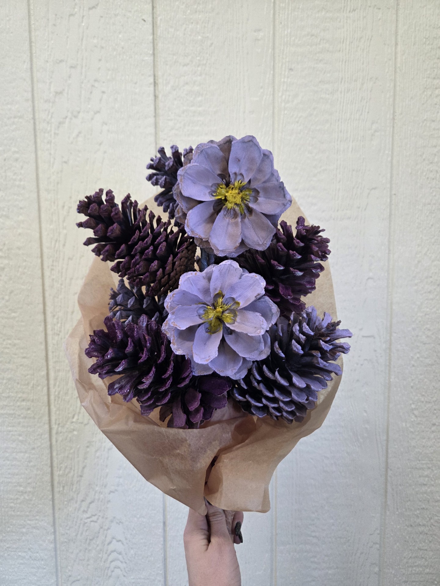 A bouquet of purple painted pinecones made to look like flowers, wrapped in paper and against a white background.