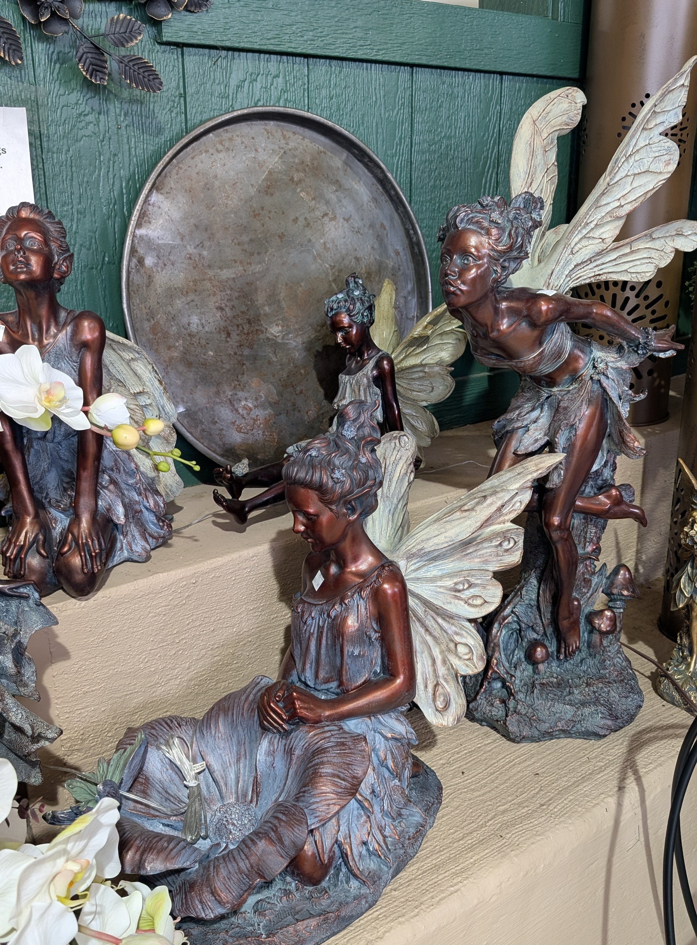 Cream steps against a green background displaying bronze looking fairy statues.