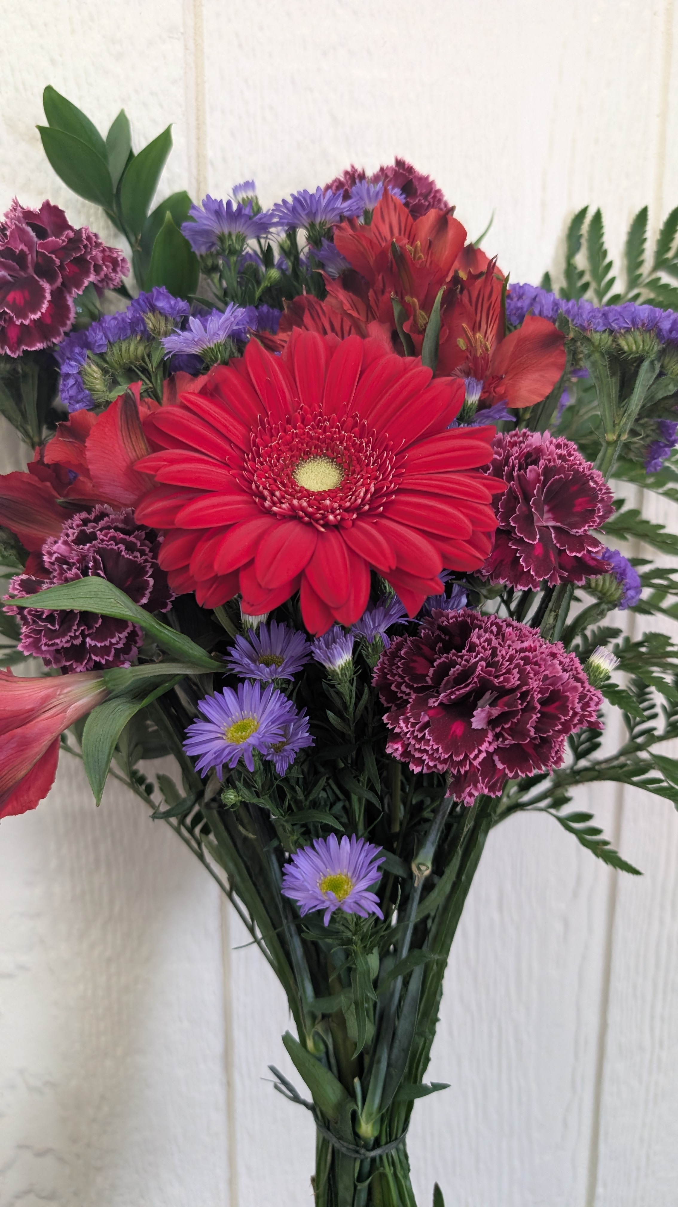 Unwrapped bouquet of red, blue, and purple flowers with greenery.