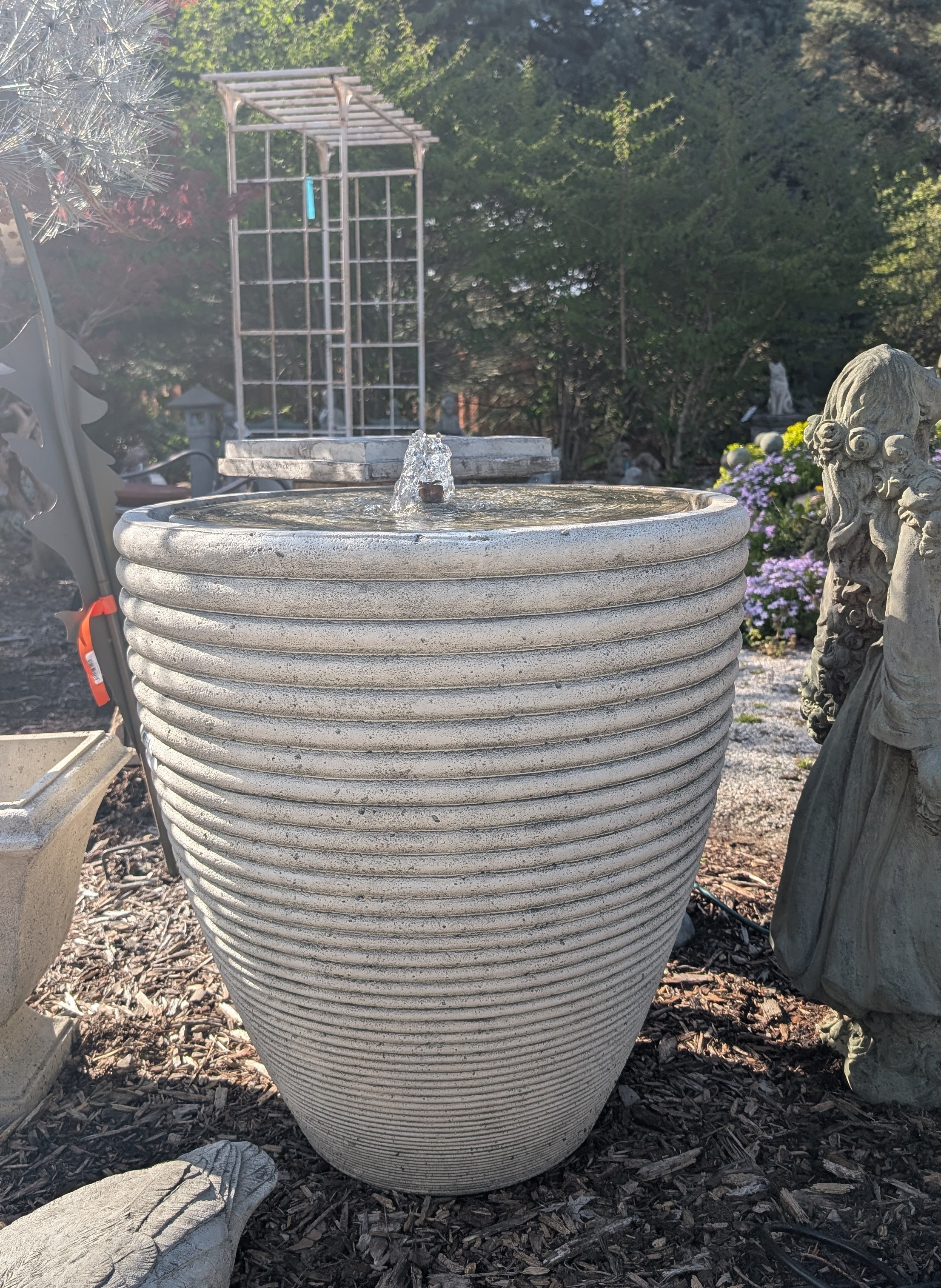 Tall egg shaped fountain with wavy texture with sunlight falling on the left side.