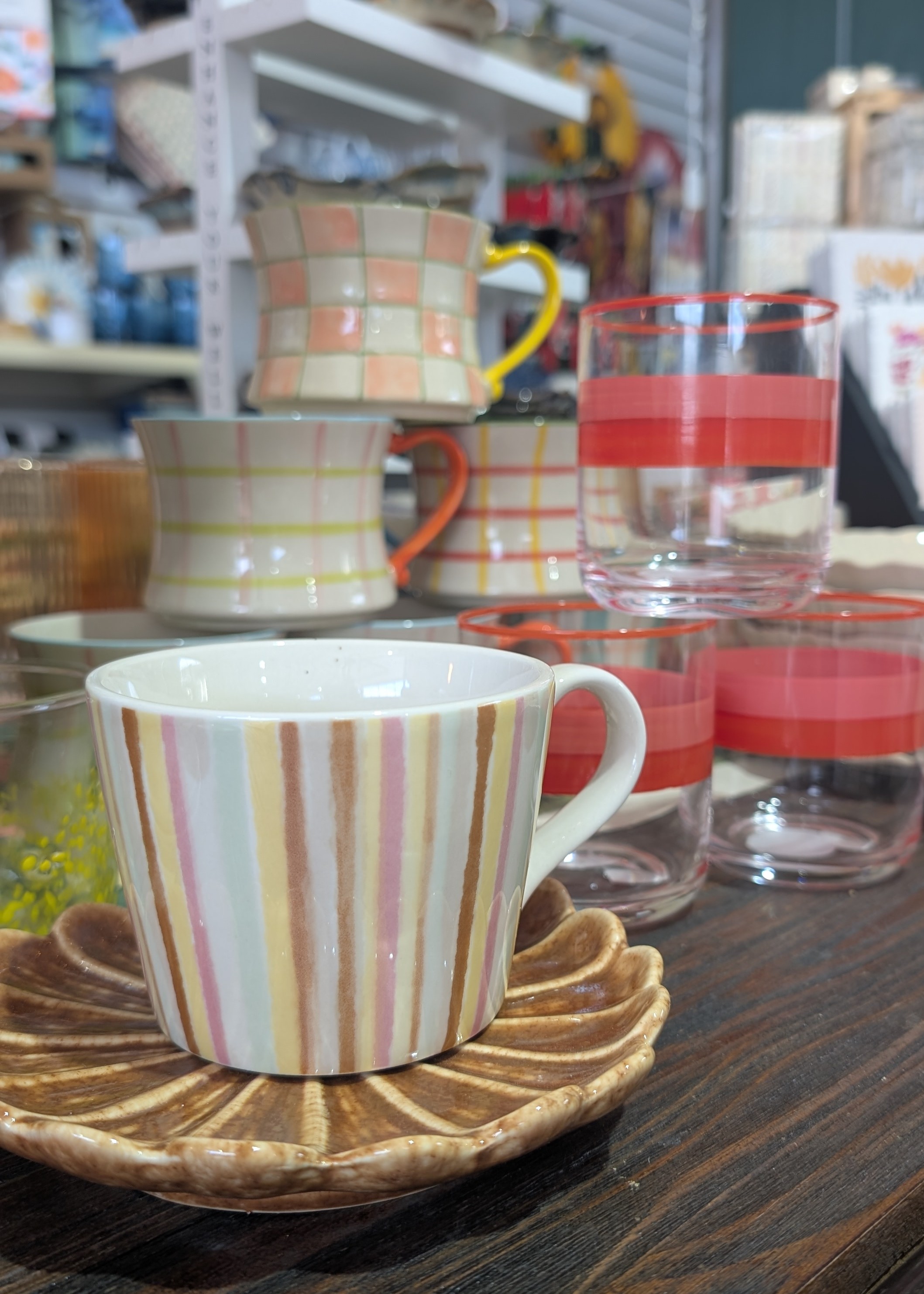 Single striped mug in the foreground with a stack of geometrically patterned mugs behind.