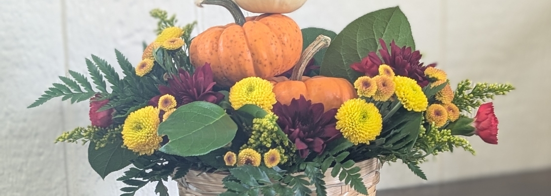 Basket of fall flowers with mini pumpkins on a wooden table with a white background.