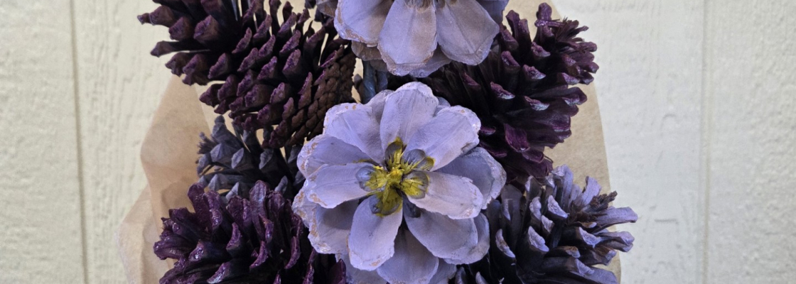 A bouquet of purple painted pinecones made to look like flowers, wrapped in paper and against a white background.